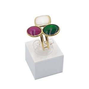 Gold-tone triple-stone ring with white, pink, and green cabochon stones on a white display stand, photographed from above.