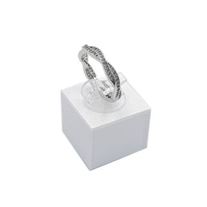 Silver ring with small dark stones on a clear display stand atop a white jewelry box, product photo, studio lighting.