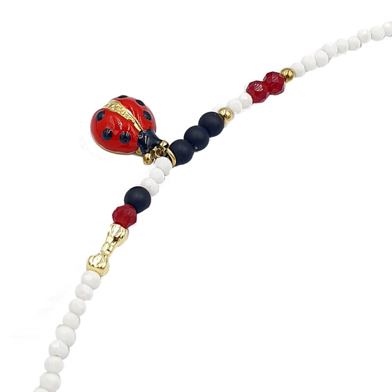 Delicate beaded bracelet featuring white round beads, a red enamel ladybug charm, and gold accents with darker navy beads.