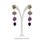 Gold-tone drop earrings with four colored stones (lavender to navy) on a white display stand.