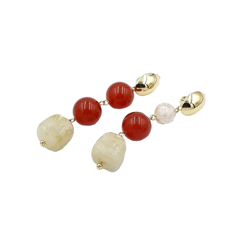 Gold-tone earrings with cream carved square beads at the ends, red round beads in the middle, and a white crystal bead near the top, connected by small gold links