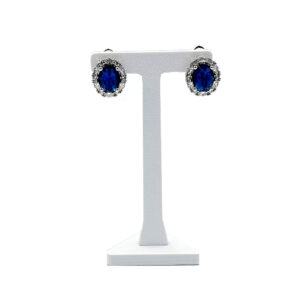 Blue oval sapphire stud earrings with a halo of small diamonds on a silver stand.