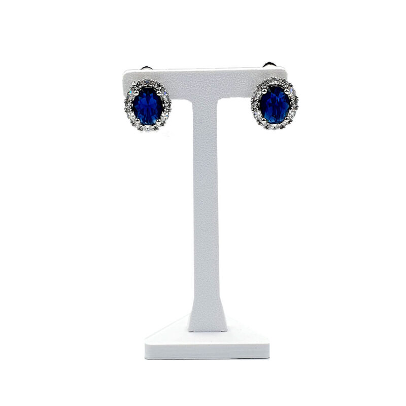 Blue oval sapphire stud earrings with a halo of small diamonds on a silver stand.