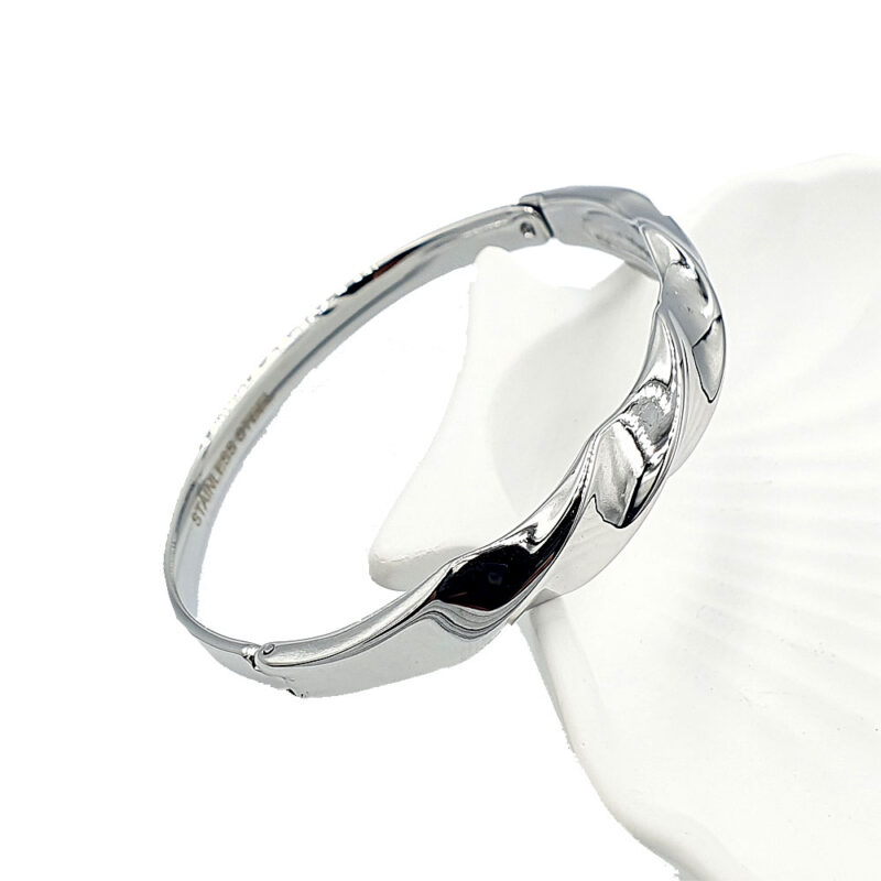 Βραχιόλι κυματιστό ασημί 2 - bijouxbijoux Shiny silver bangle bracelet with curved links resting on a white display surface against a white background.