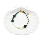 Bracelet with dark green beads and white freshwater pearls, gold spacers and clasp, arranged in a partial circle on a white shell dish.