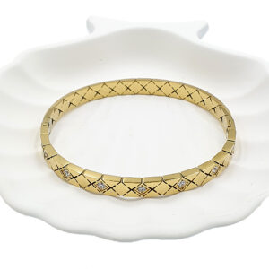 Βραχιόλι χειροπέδα με στρας - bijouxbijoux Gold bracelet with geometric crisscross pattern and diamond accents on a white ceramic dish.