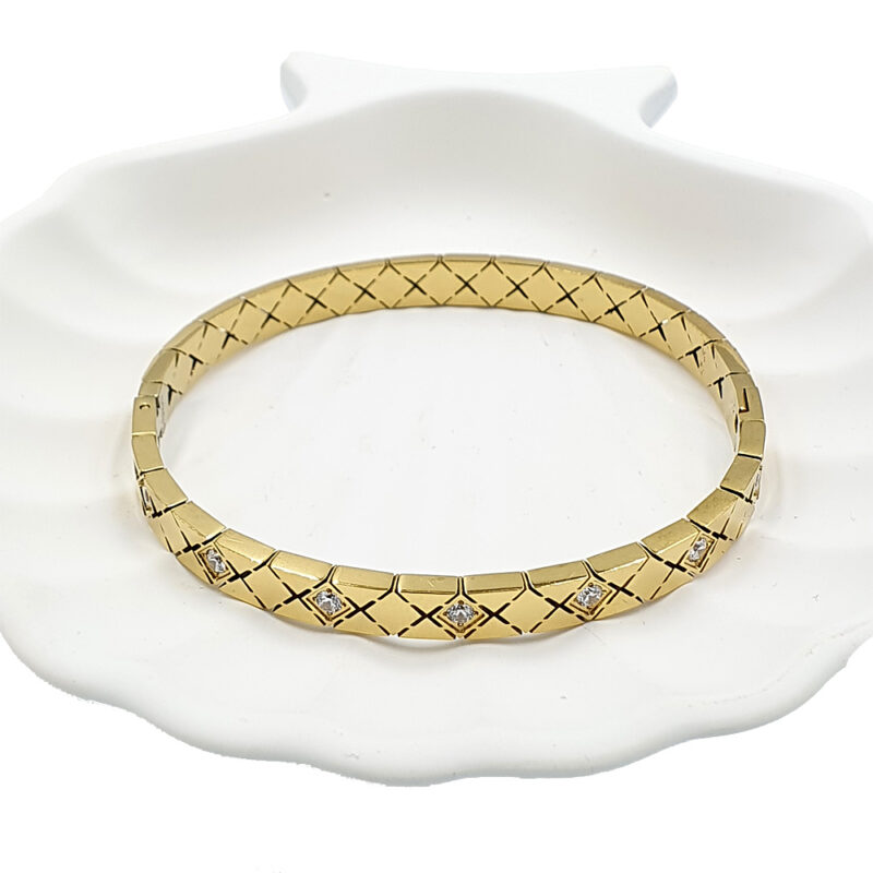 Gold bracelet with geometric crisscross pattern and diamond accents on a white ceramic dish.