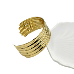 Εντυπωσιακό χρυσαφί βραχιόλι 2 - bijouxbijoux Gold multi-band cuff bracelet resting on a white plate, shown from the side to highlight its open-ended design.