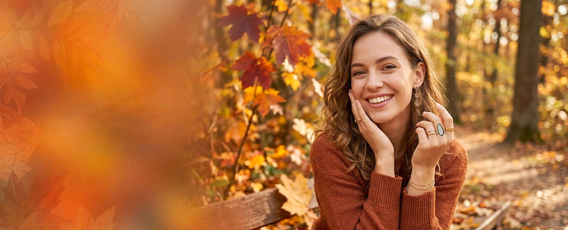 Smiling woman in a rust sweater sits on a park bench amid autumn leaves and warm sunlight.